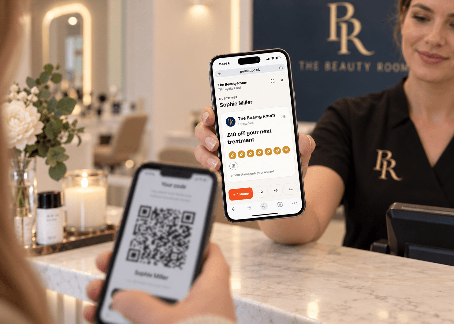 Behind the till at The Beauty Room, a member of staff holds a phone showing Sophie Miller's loyalty card at 7 of 8 stamps in the Perklet till view, with a “+1 stamp” button, while the customer holds up the Perklet code on their own phone.