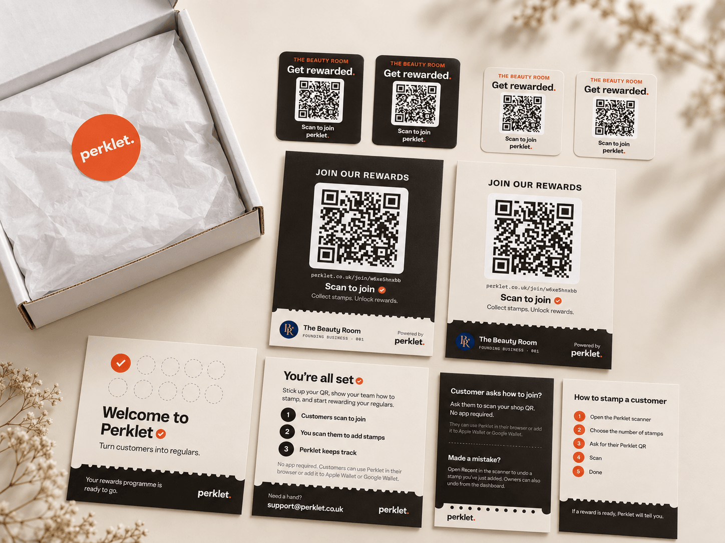 The Perklet Welcome Pack laid out: an open box with a perklet sticker, two dark and two light join-QR stickers, dark and light A6 counter cards printed in the shop's name, a welcome card and a quick-start guide.